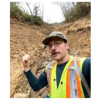 Dr Phillip Prince standing in front of a landslide area and gesturing towards it