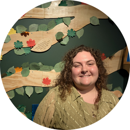 Zoya with curly hair standing in front of the plywood tree in Our Changing World